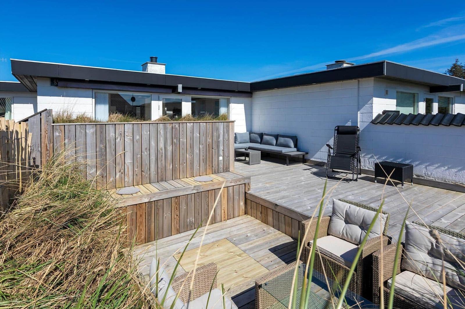 Terrasse mit Sitzgelegenheiten und Holzgeländer. Hintergrund: modernes Haus mit weißer Fassade.