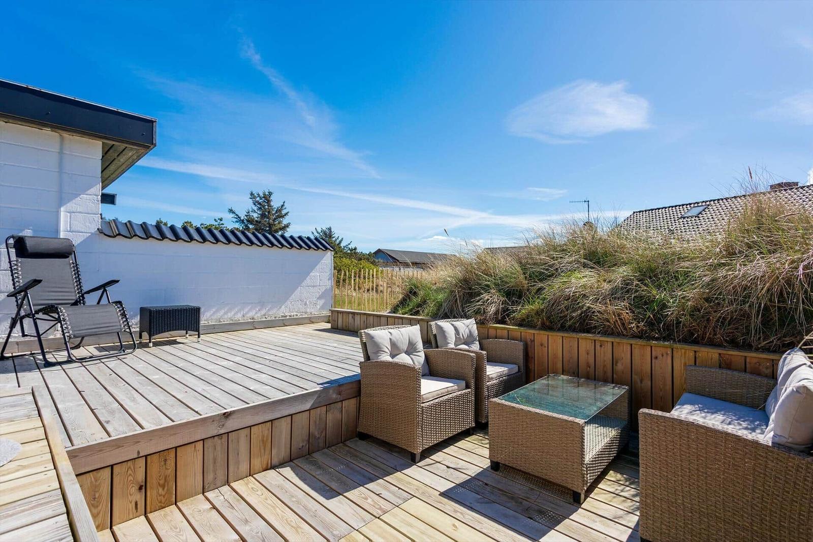 Terrasse mit Sitzgruppe und Liegestuhl, Blick auf Grasland und Himmel.
