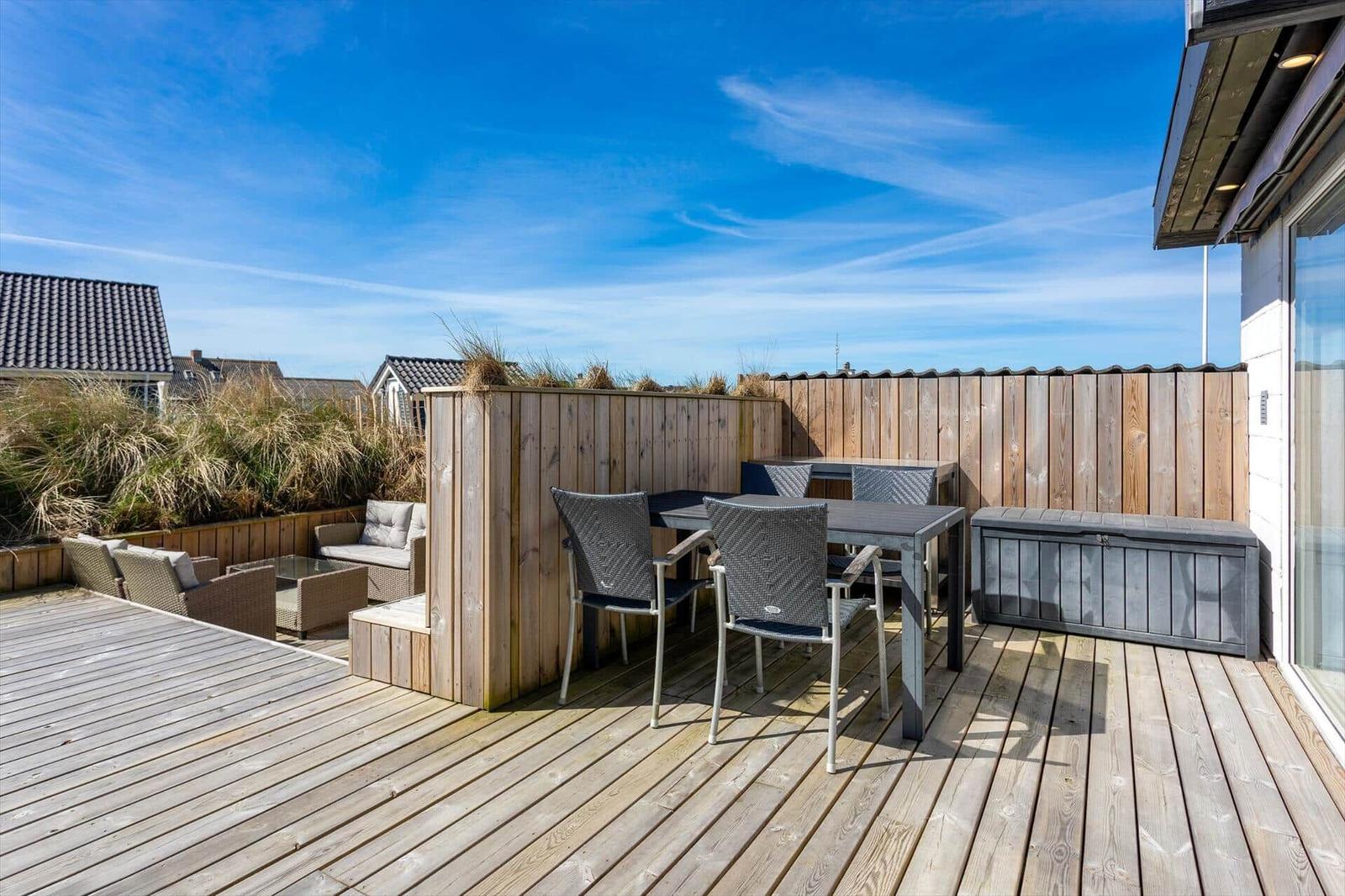 Terrasse mit Holzdecke, Sitzgruppe und Tisch. Hintergrund: Holzzaun und Gras.