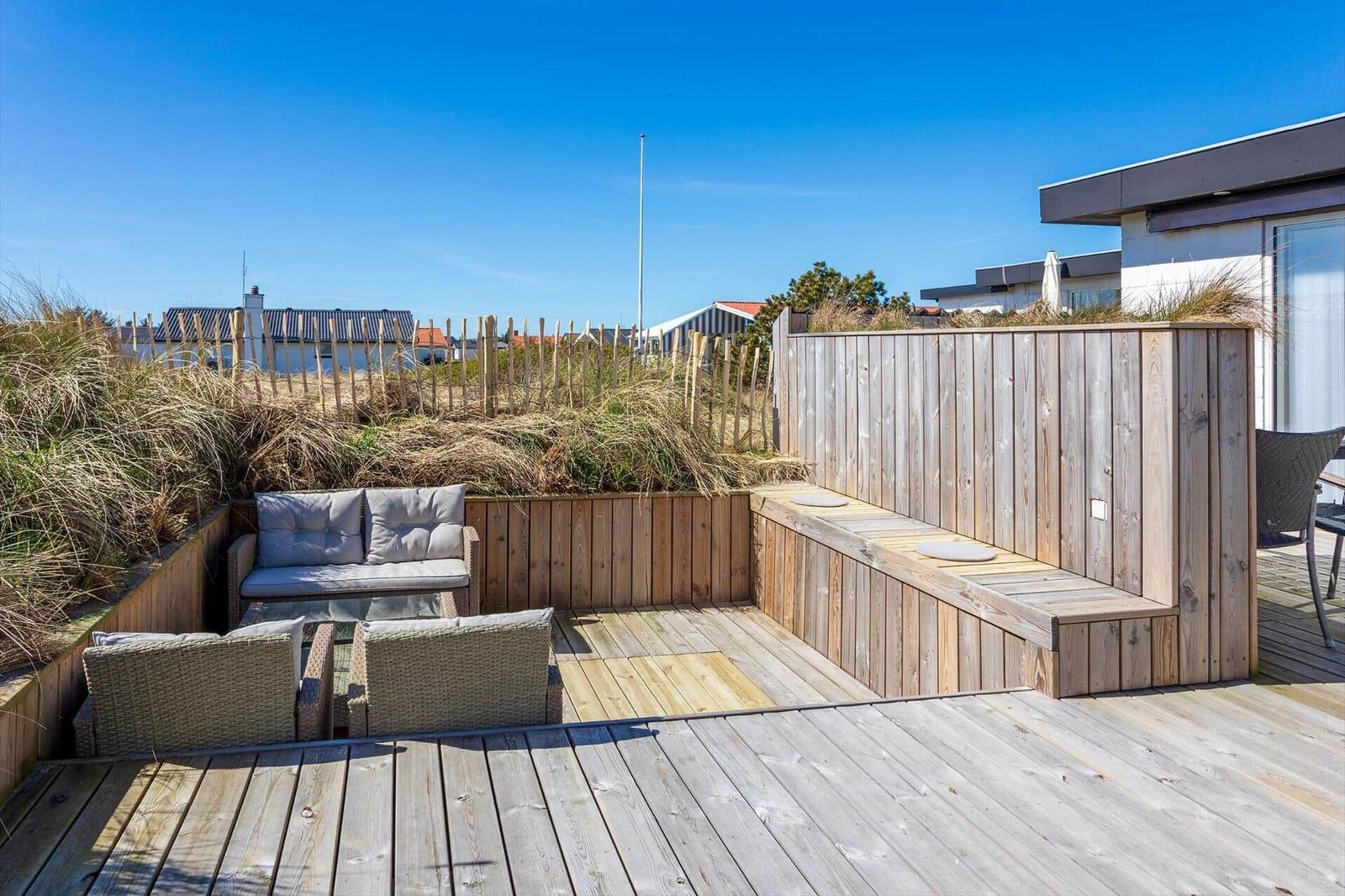 Terrasse mit Holzbank, Sitzgruppe und Blick auf Dünen.