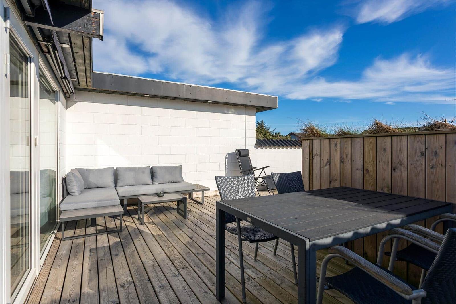 Terrasse mit Holzdecke, Sitzgruppe und Tisch mit Stühlen unter blauem Himmel.