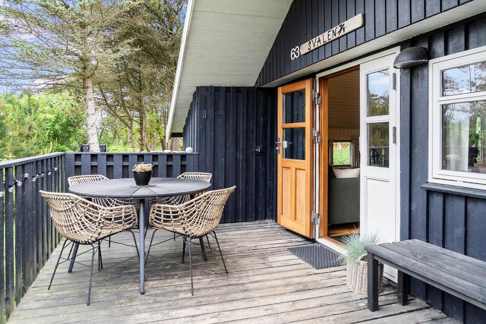 Deck with table and chairs in front of a house with wooden door and window.