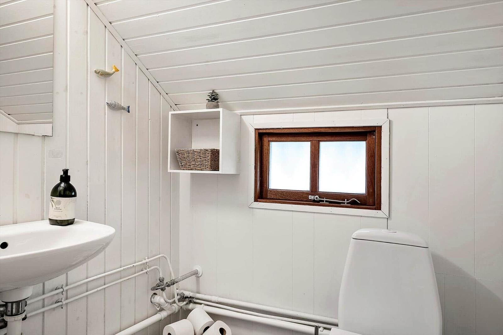 Bathroom with sink, toilet, and window with wooden frame.