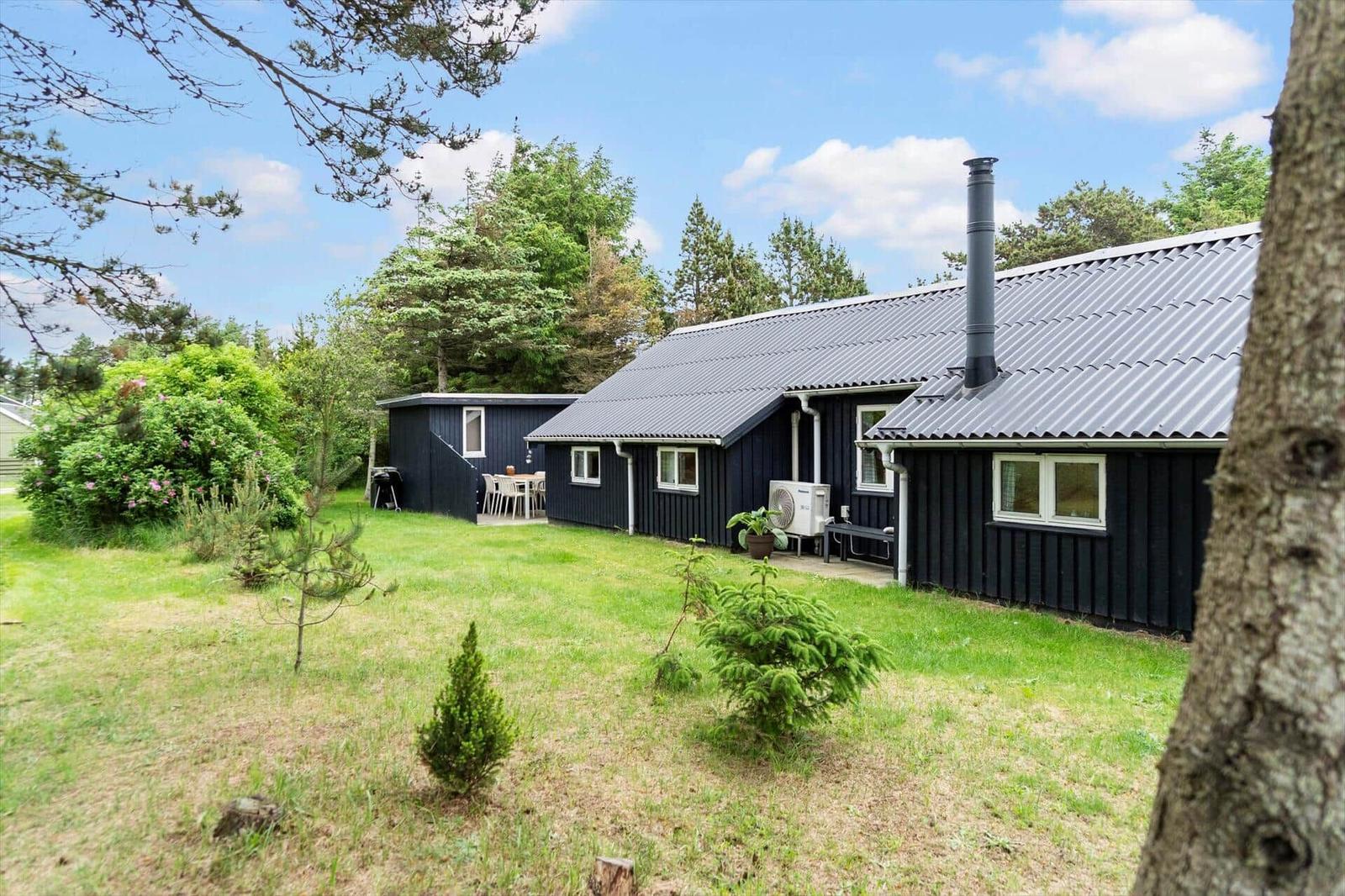 Black cabin with garden and barbecue area. Wooden siding and metal roof.