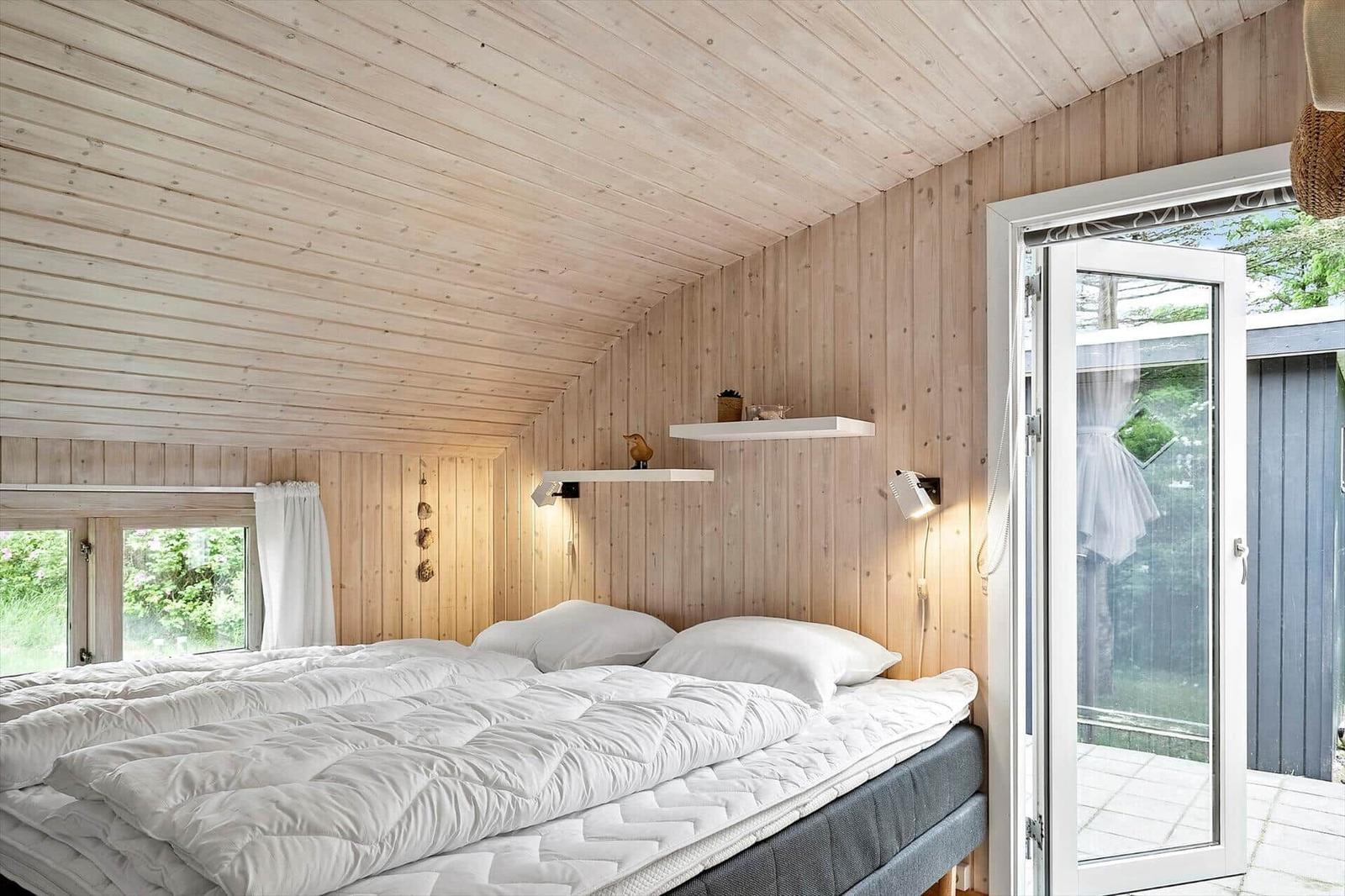 Bedroom with wooden walls and ceiling, white bed, and sliding door to balcony.