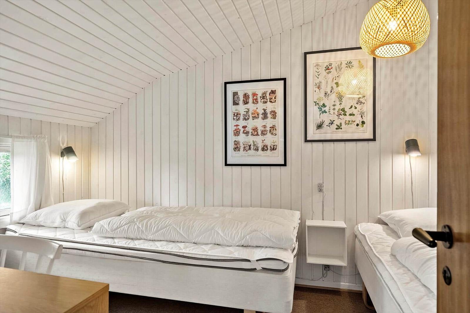 Room with two beds, white walls, and wooden ceiling. Two framed pictures hang on the walls.