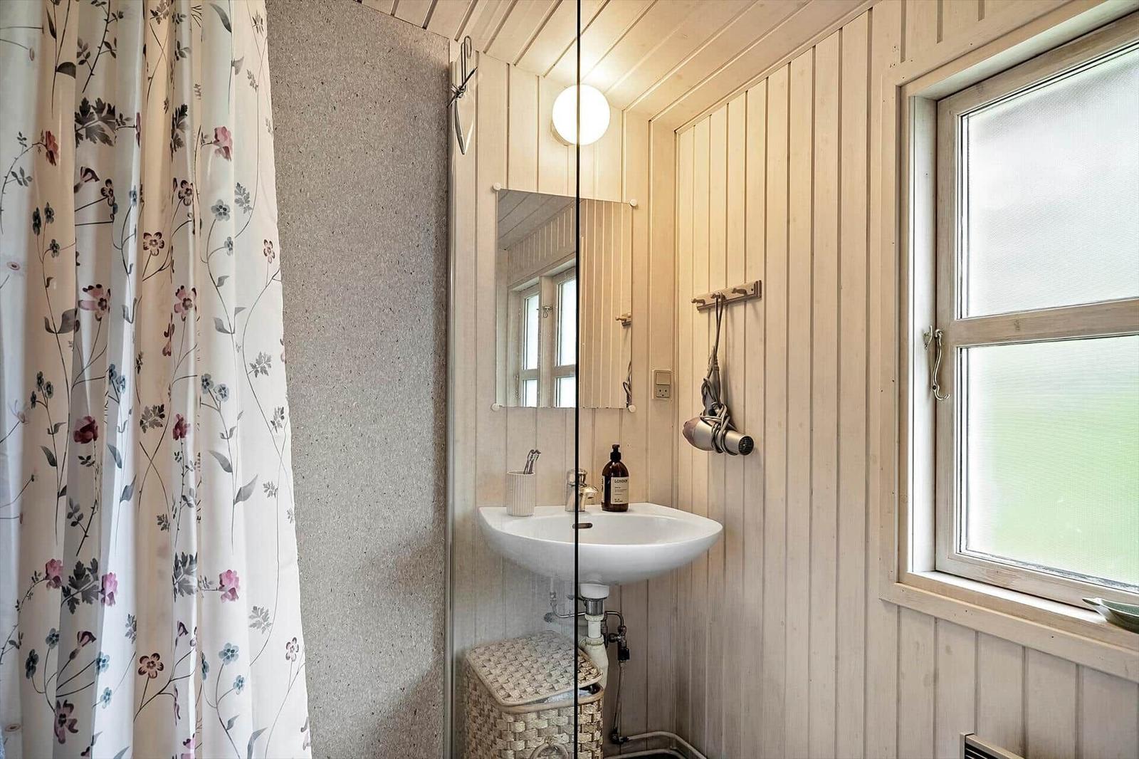 Bathroom with sink, mirror, and window. Shower curtain with floral pattern.