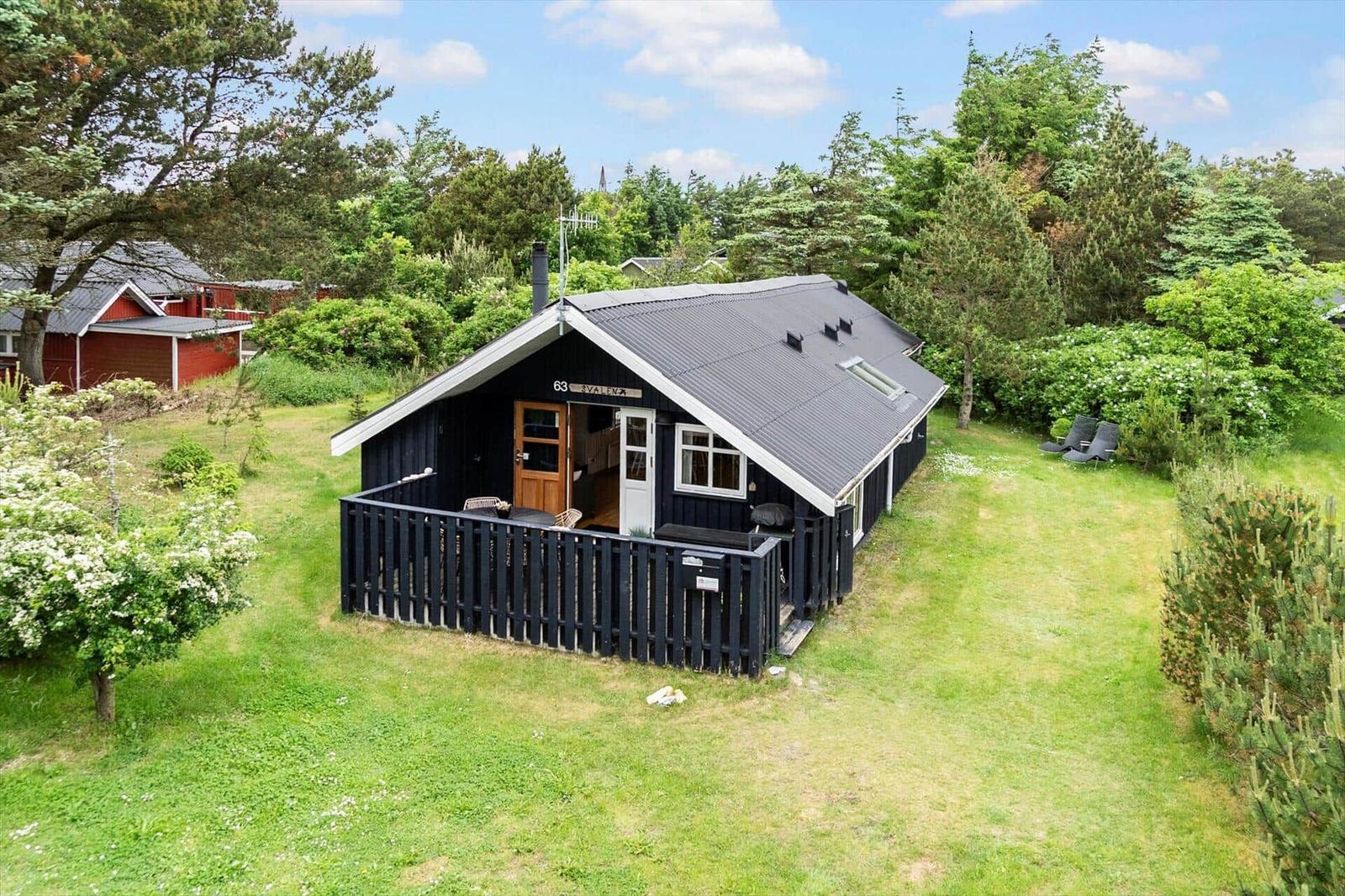 Black wooden house with balcony, surrounded by lawn and trees.