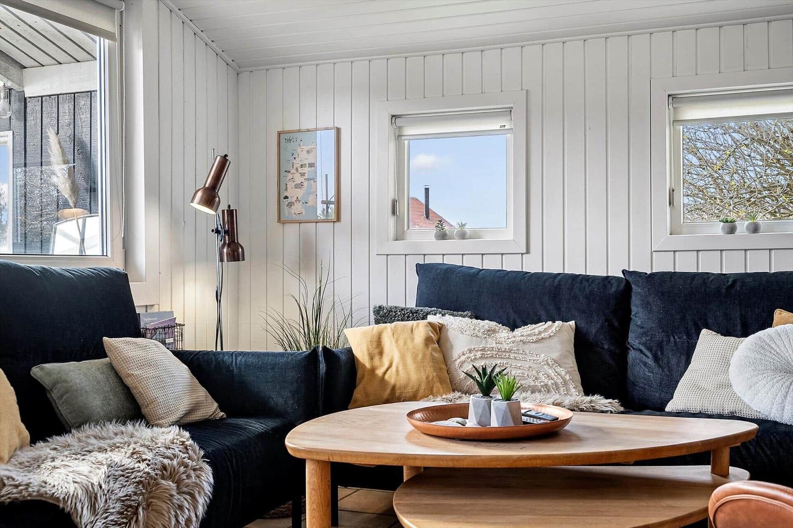 Wohnzimmer mit dunklem Sofa, Holztisch und Fenstern mit Blick.