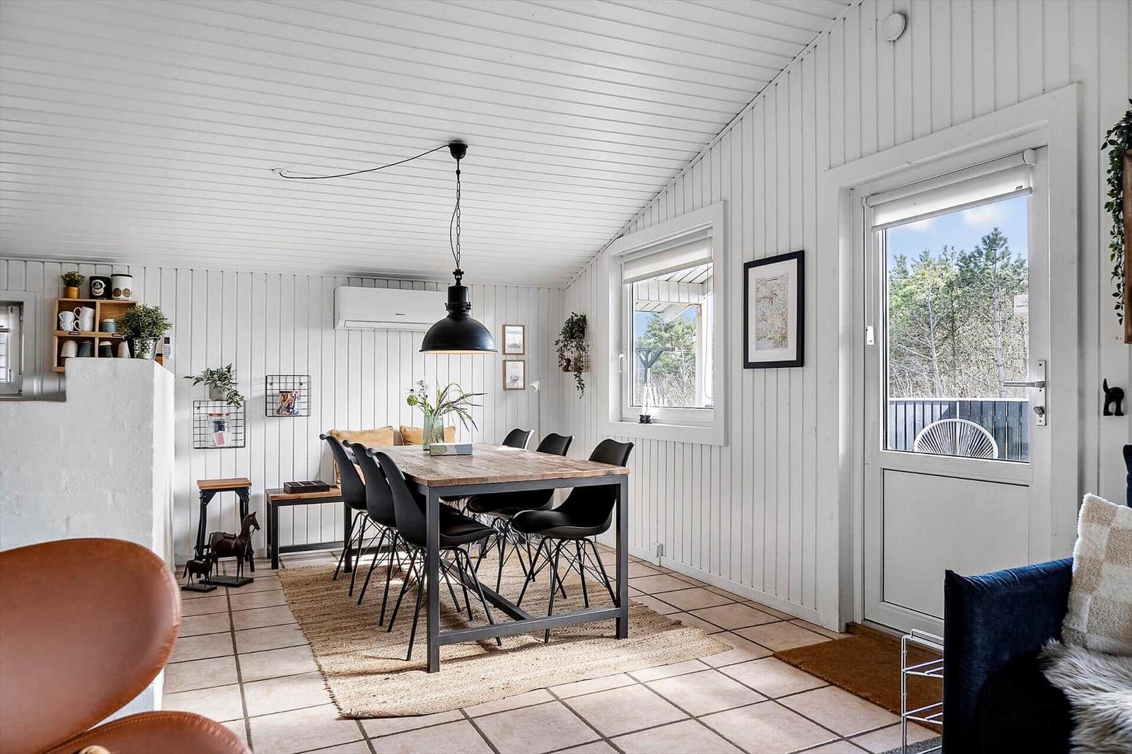 Essbereich mit Holztisch, schwarzen Stühlen und Fenster zur Terrasse.