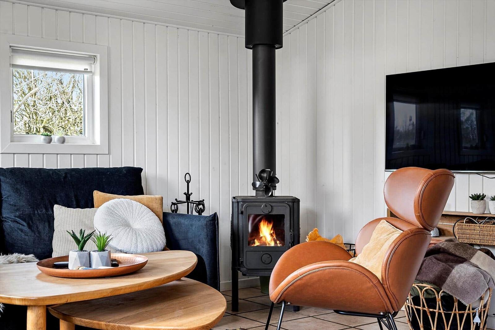 Ein Wohnzimmer mit Kaminofen, Ledersessel und Holztisch. An der Wand hängt ein Fernseher.