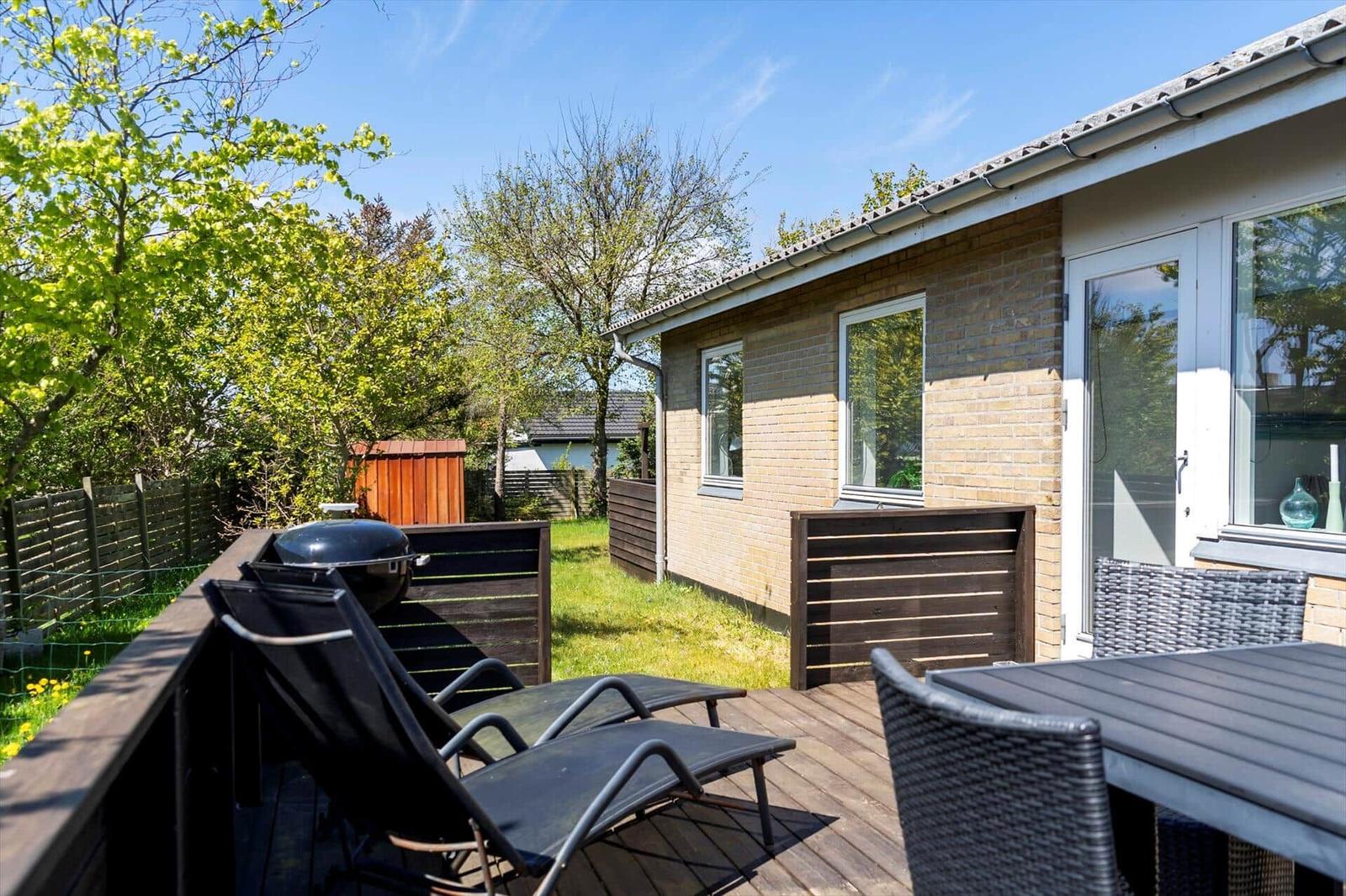 Terrasse mit Liegen, Tisch und Grill. Hinterhof mit Grünfläche und Bäumen.