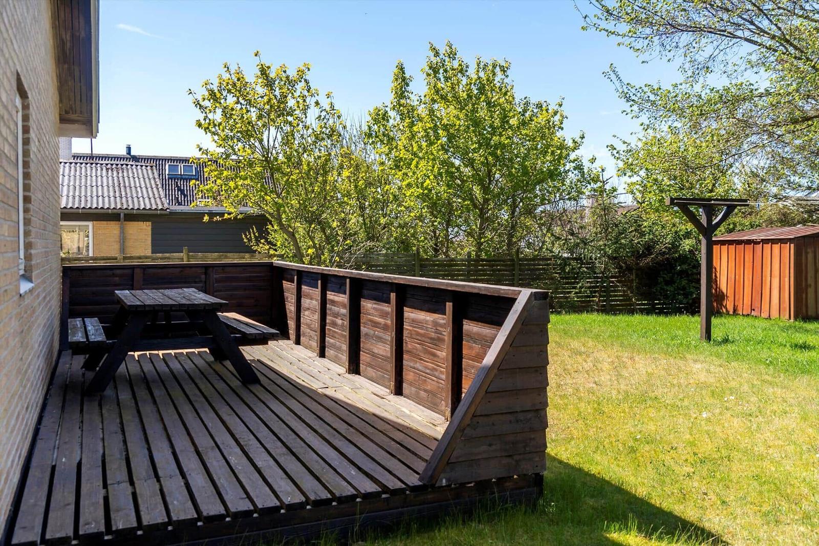 Holzterrasse mit Picknicktisch und Grünfläche im Hintergrund.