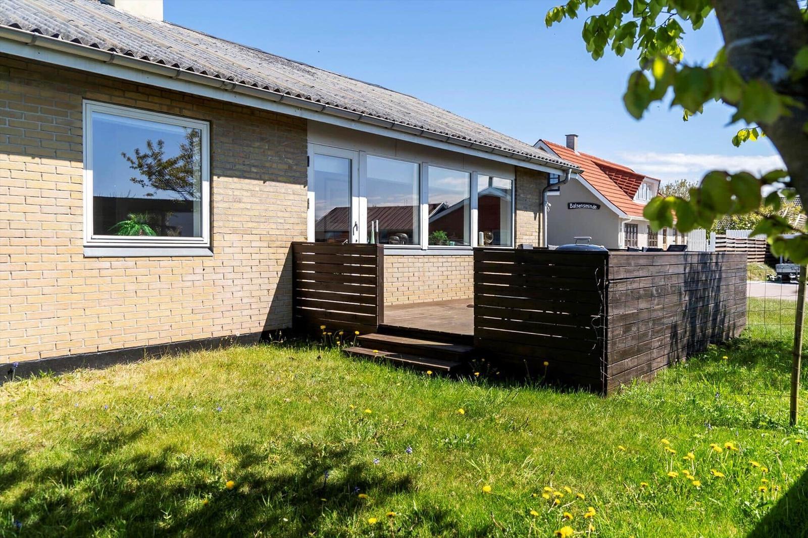 Ein Haus mit Holzterrasse und Grünfläche. Im Hintergrund steht ein weiteres Haus.