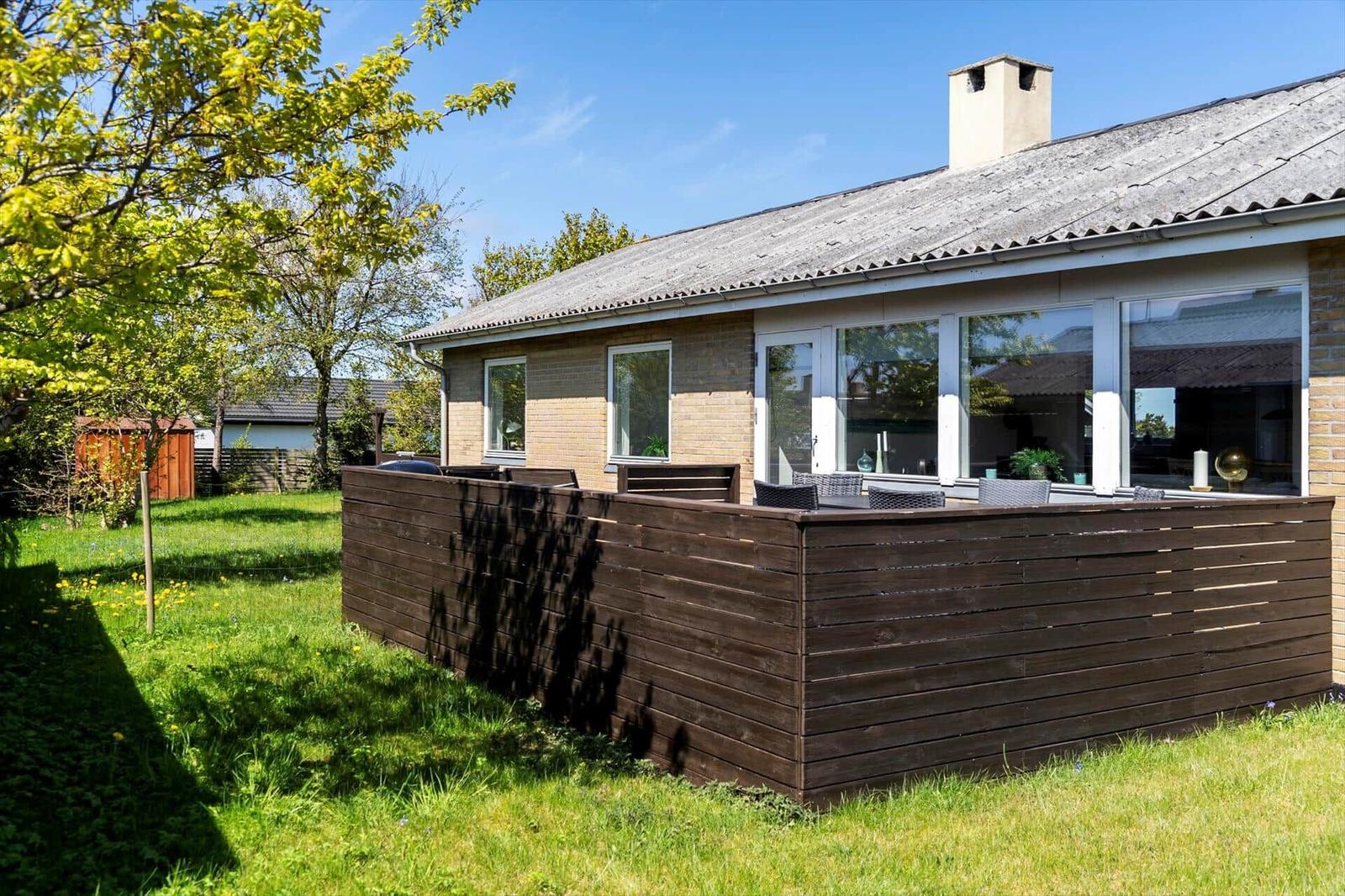 Haus mit Holzterrasse und großem Fensterbereich im Garten.