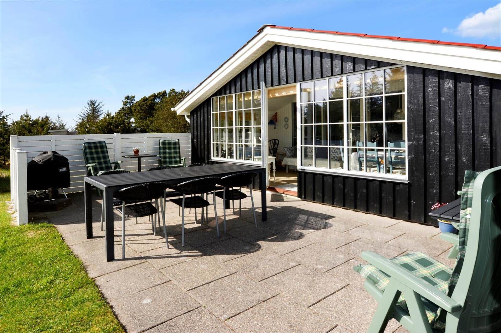 Terrasse mit Tisch, Stühlen und Grill neben einem Haus mit großen Fenstern.