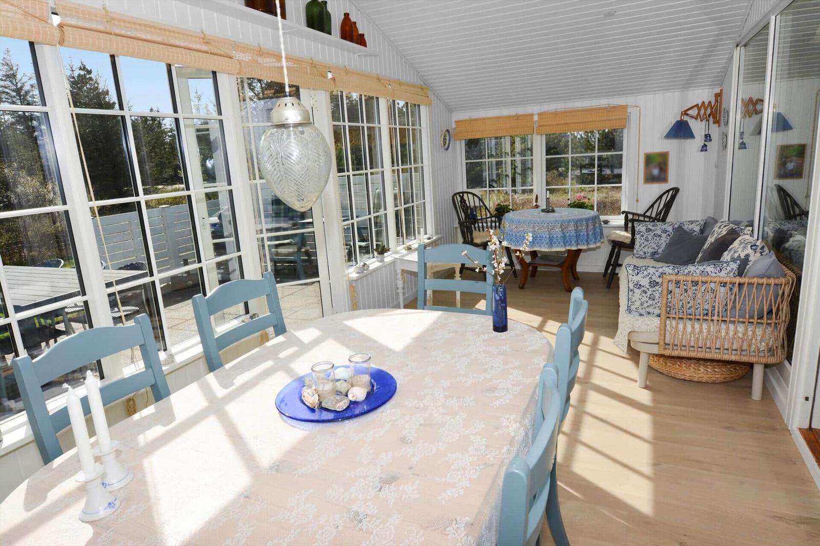 Esszimmer mit runder Tisch und blauen Stühlen, großes Fenster, Sitzgruppe mit Wicker-Sofa.
