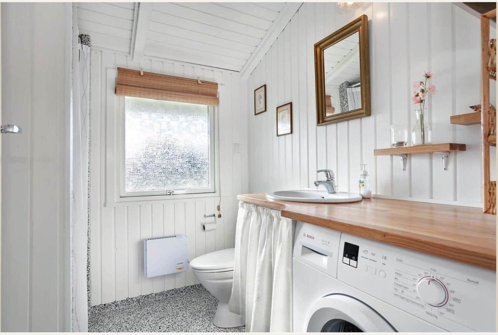 Badezimmer mit Waschmaschine, Spiegel und Fenster mit Rollladen.