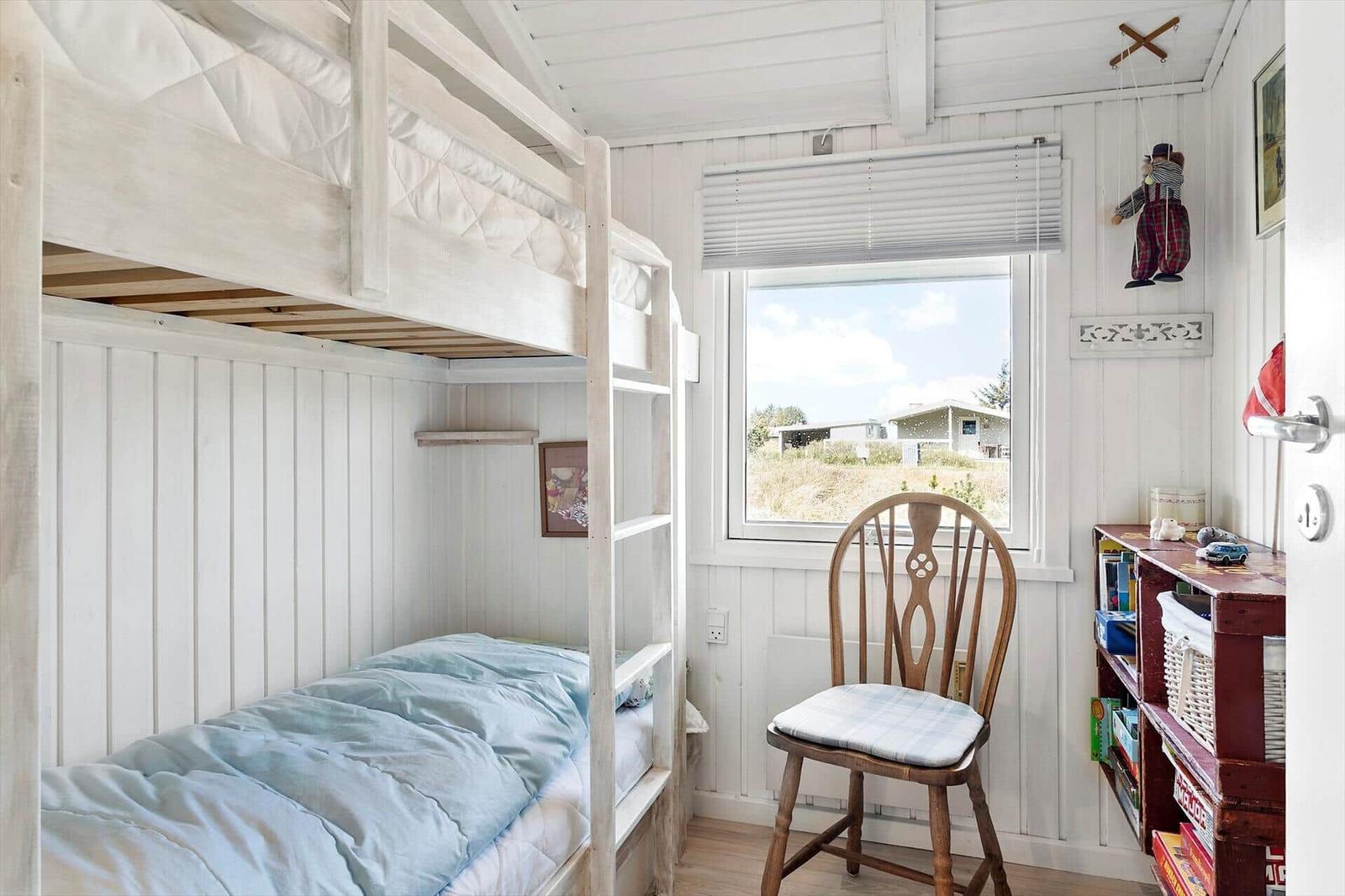 Kinderzimmer mit Doppelstockbett, Stuhl und Bücherregal. Fenster zeigt Außenbereich.