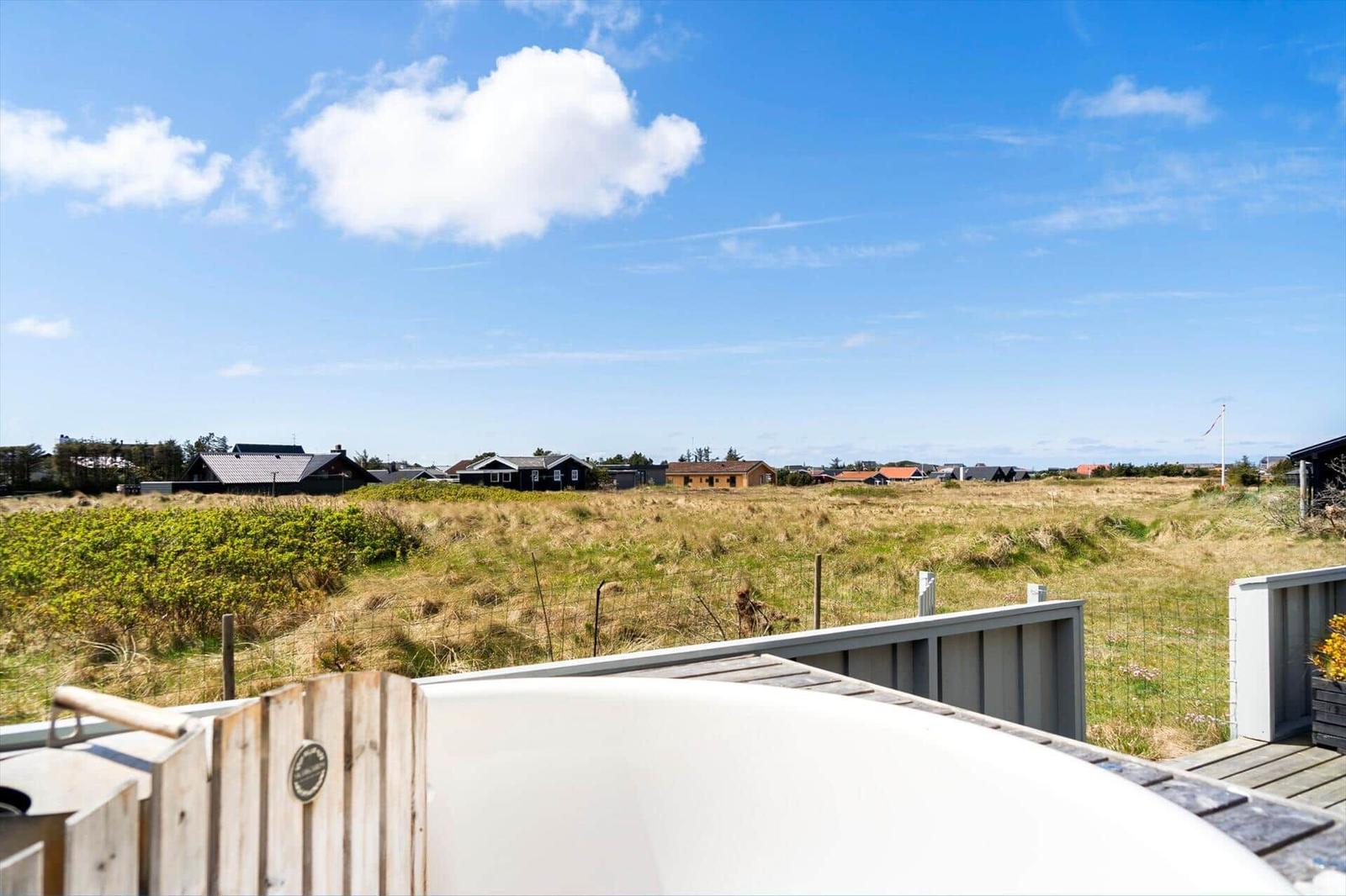 Whirlpool auf Terrasse mit Blick auf Grasland und Häuser im Hintergrund unter blauem Himmel.