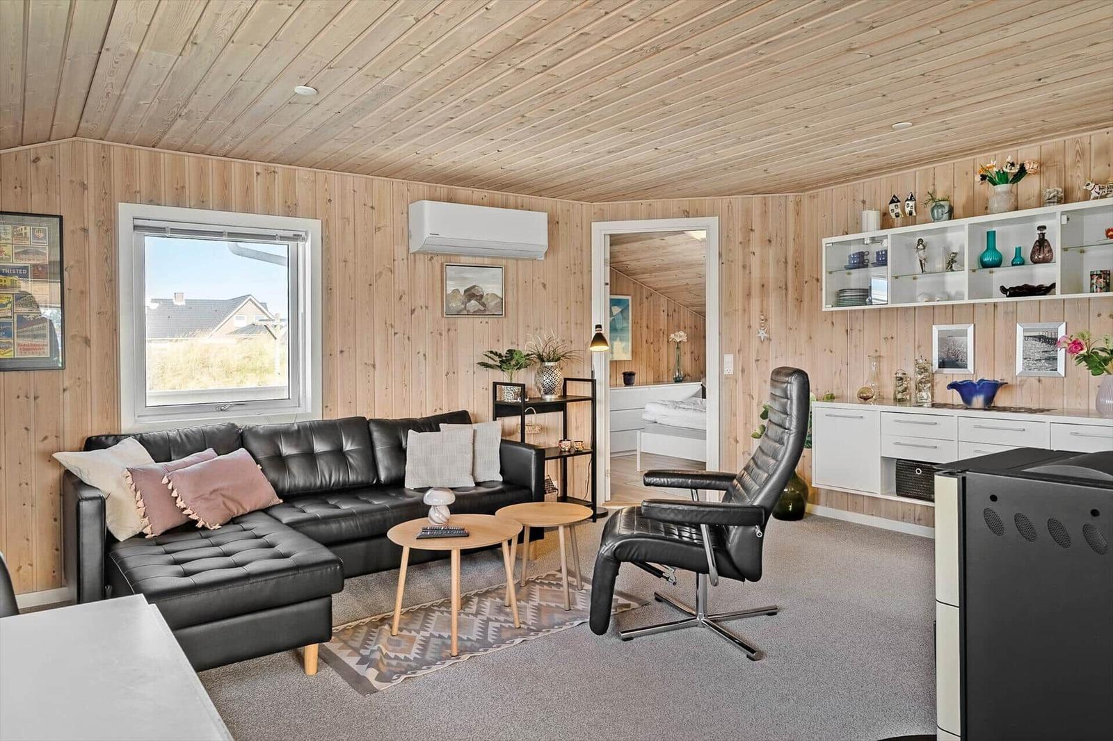 Wohnzimmer mit Sofa, Sessel und Küchenzeile. Holzwände und -decke. Blick auf das Schlafzimmer.
