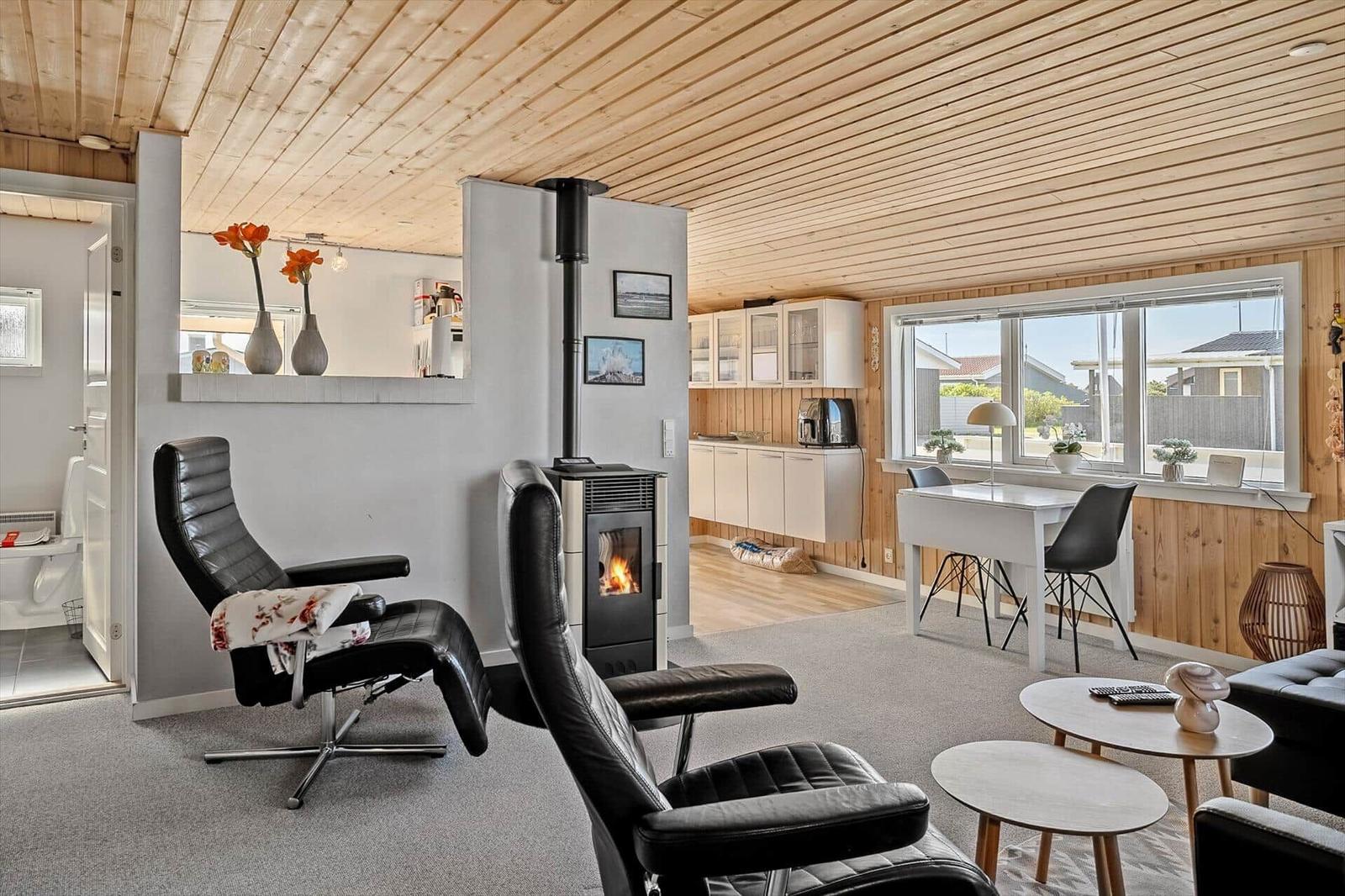 Wohnraum mit Kamin, zwei schwarzen Sesseln und Blick auf Küche und Fensterbereich.