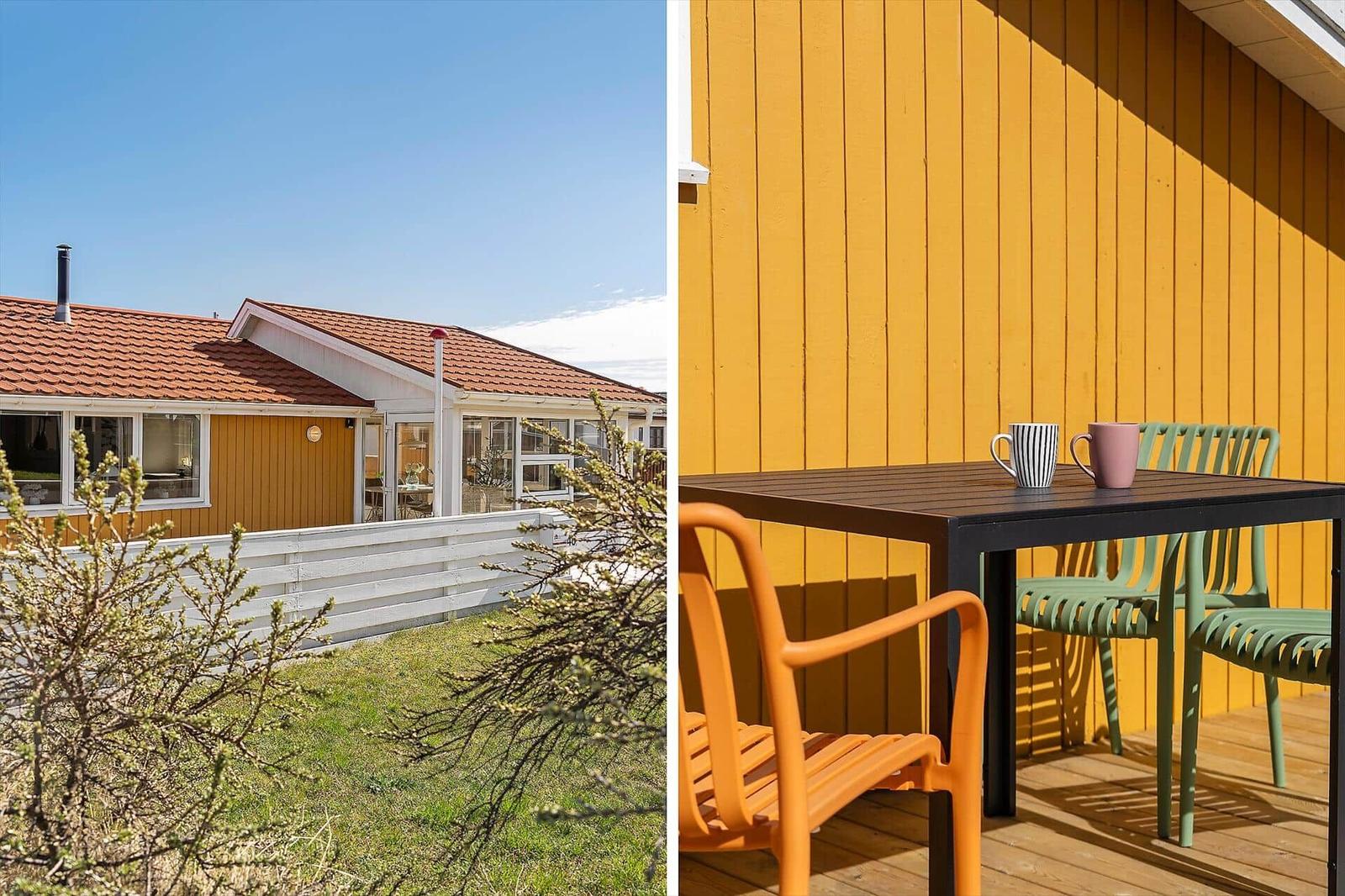 Haus mit gelbem Holzschuppen und Terrasse mit Tisch und Stühlen.