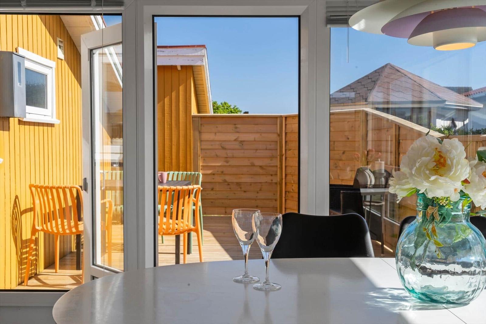 Tisch mit Gläsern und Blumen vor Fenster mit Blick auf Terrasse und Holzzaun.