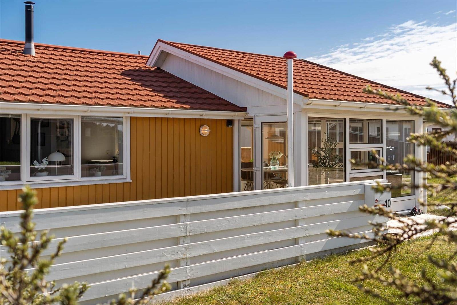 Haus mit rotem Dach, weißer Umrandung und Holzwand. Blick ins Innere durch Fenster.
