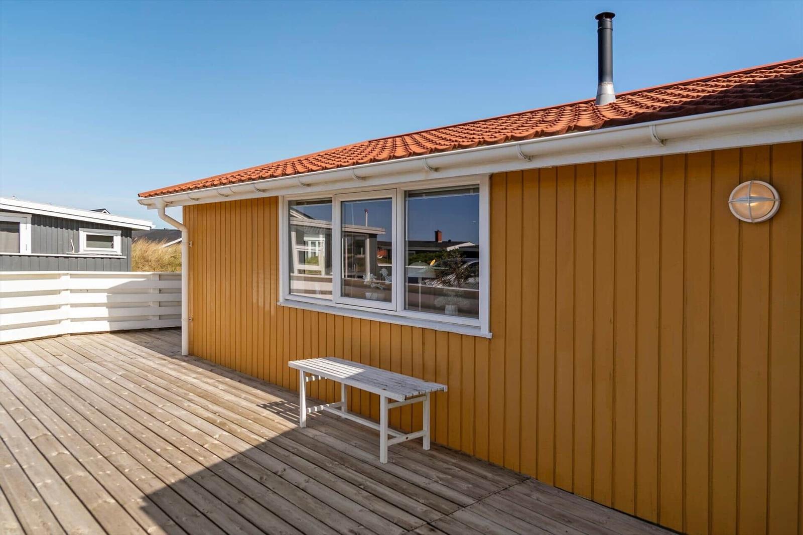 Holzveranda mit weißem Tisch vor gelbem Haus mit rotem Dach.
