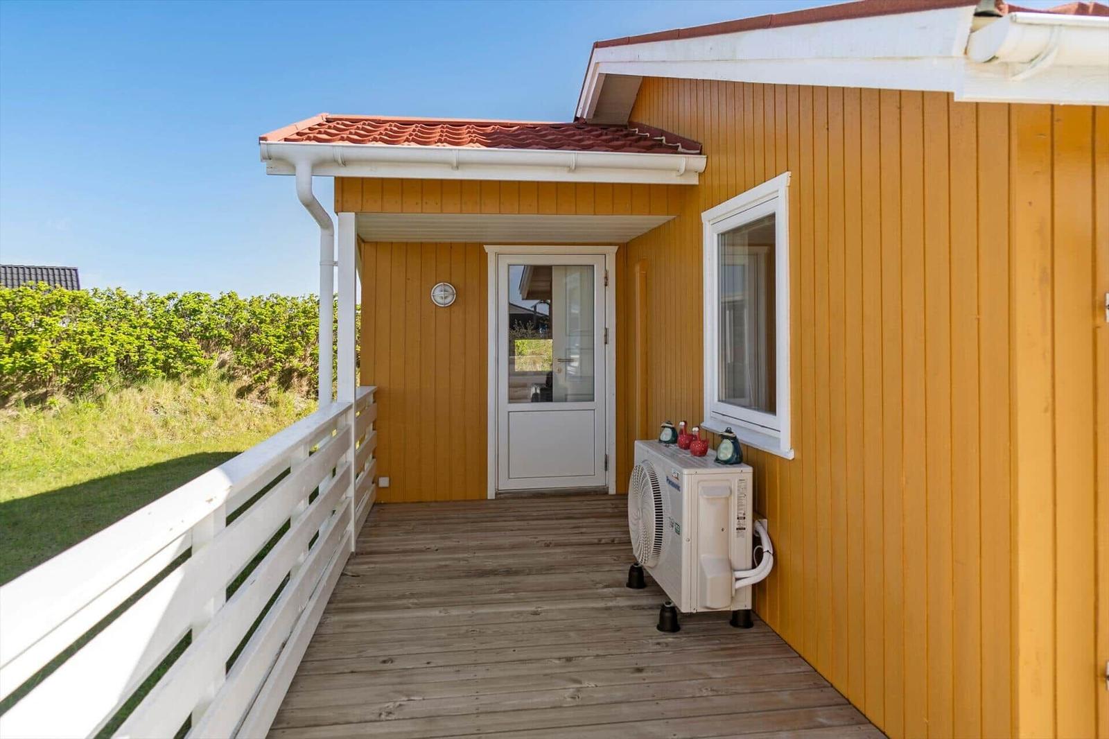 Holzveranda mit weißer Brüstung und Tür zum Haus. Außengerät an der Wand.