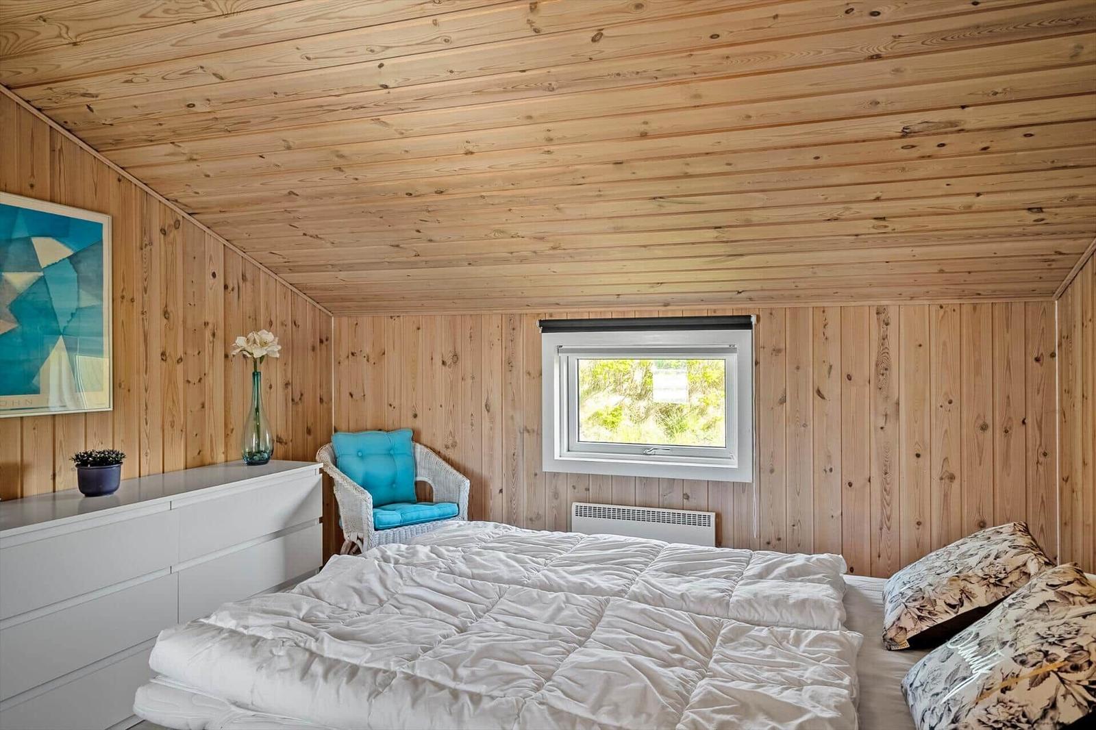 Schlafzimmer mit Holzwand, Bett, Stuhl und Fenster.