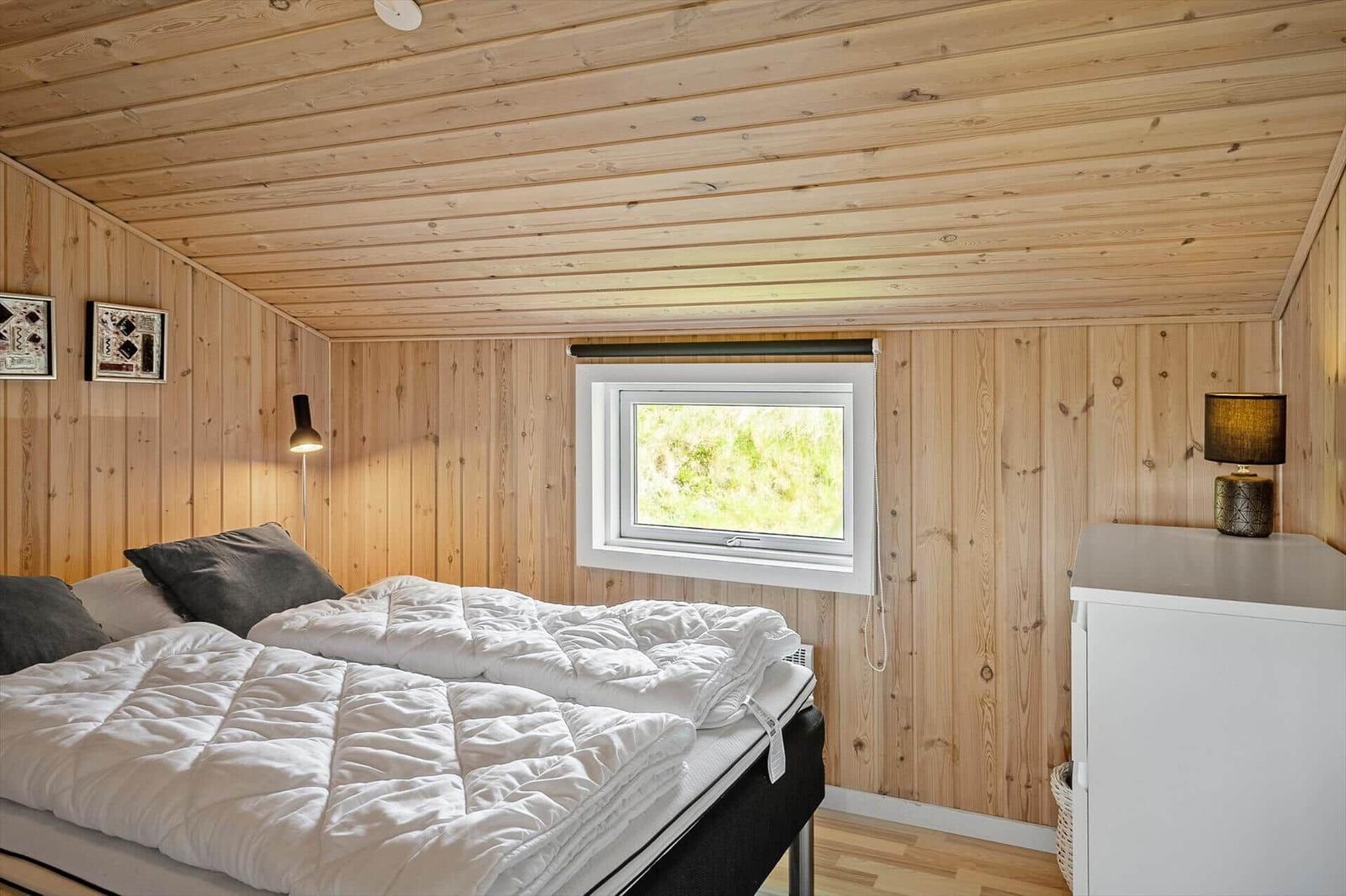 Schlafzimmer mit Holzwand, Bett, Fenster und Schrank.