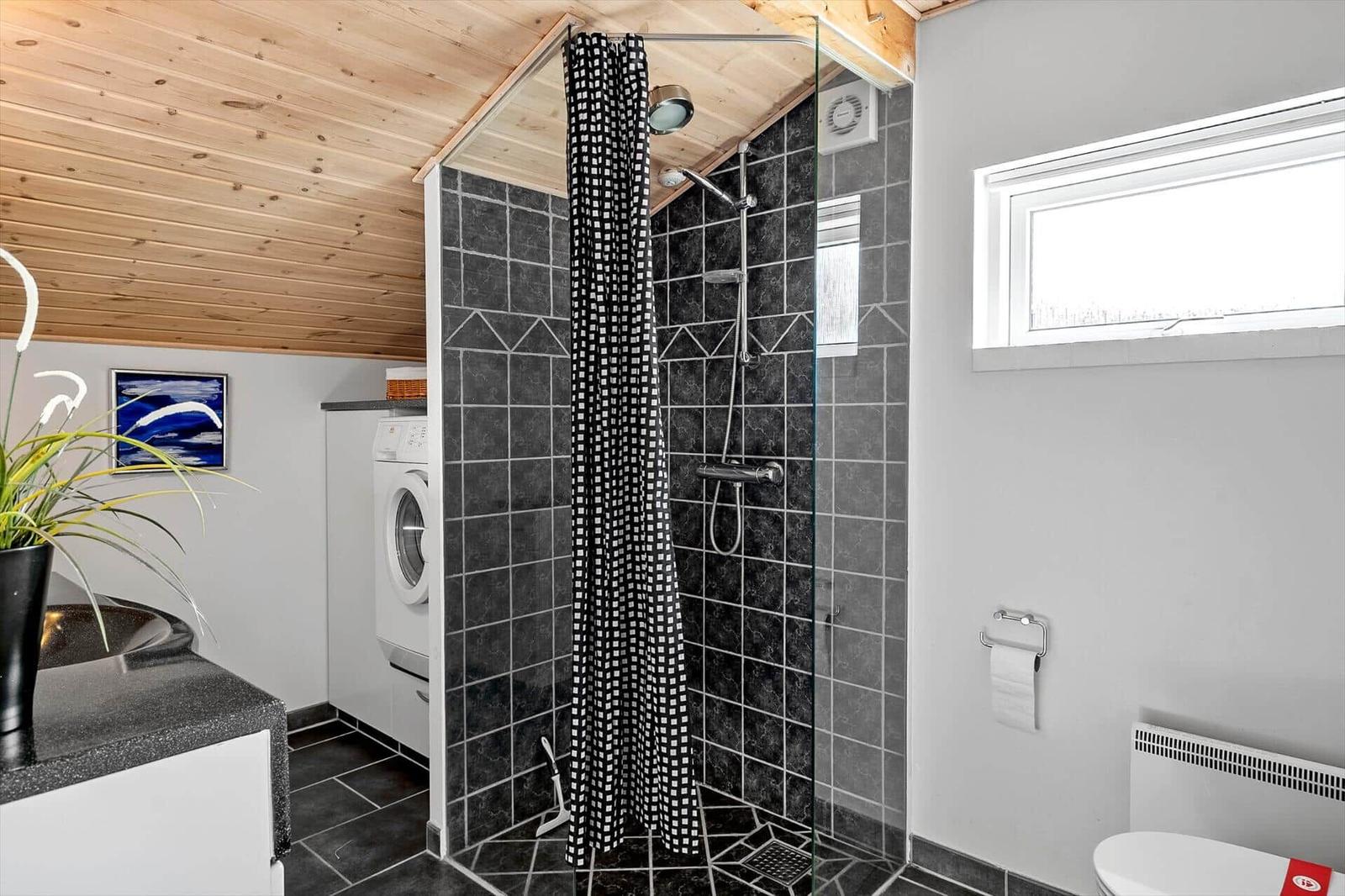 Badezimmer mit Dusche, Waschmaschine und Toilette unter Holzdecke.