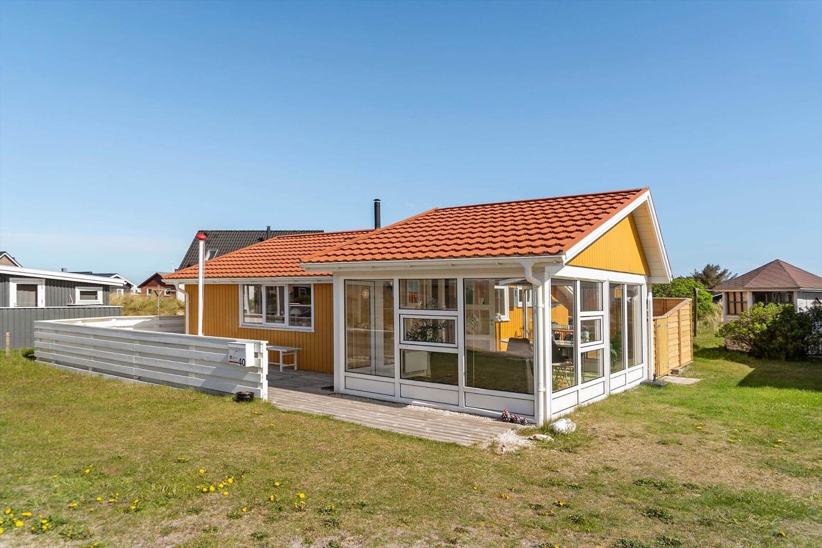 Ein Haus mit gelbem Holz und rotem Dach. Große Fenster und eine Terrasse.