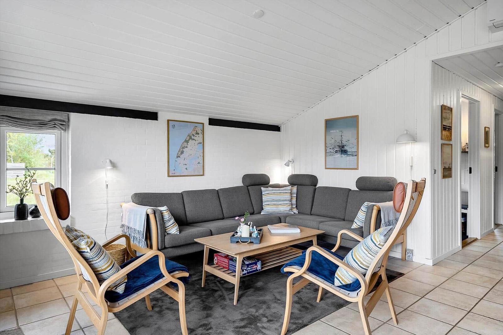 Ein Wohnzimmer mit grauem Sofa, zwei Holzstühlen und einem Holztisch.