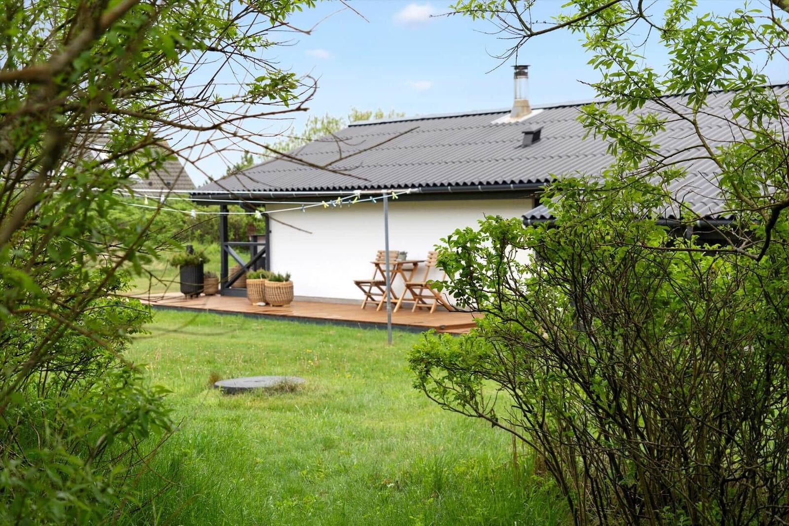 Wohnhaus mit Terrasse und Garten. Holztisch, Stühle und Pflanzen sind sichtbar.