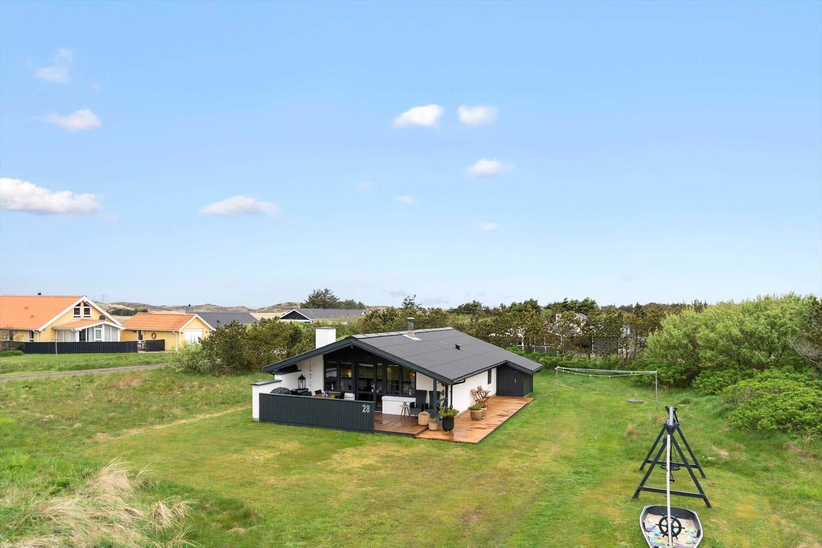 Moderne Villa mit Terrasse, umgeben von Grünflächen und Bäumen unter blauem Himmel.