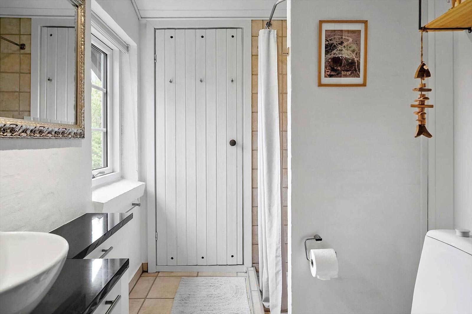 Badezimmer mit Waschbecken, Dusche und Toilette. Weiße Türen und Wandverkleidung.