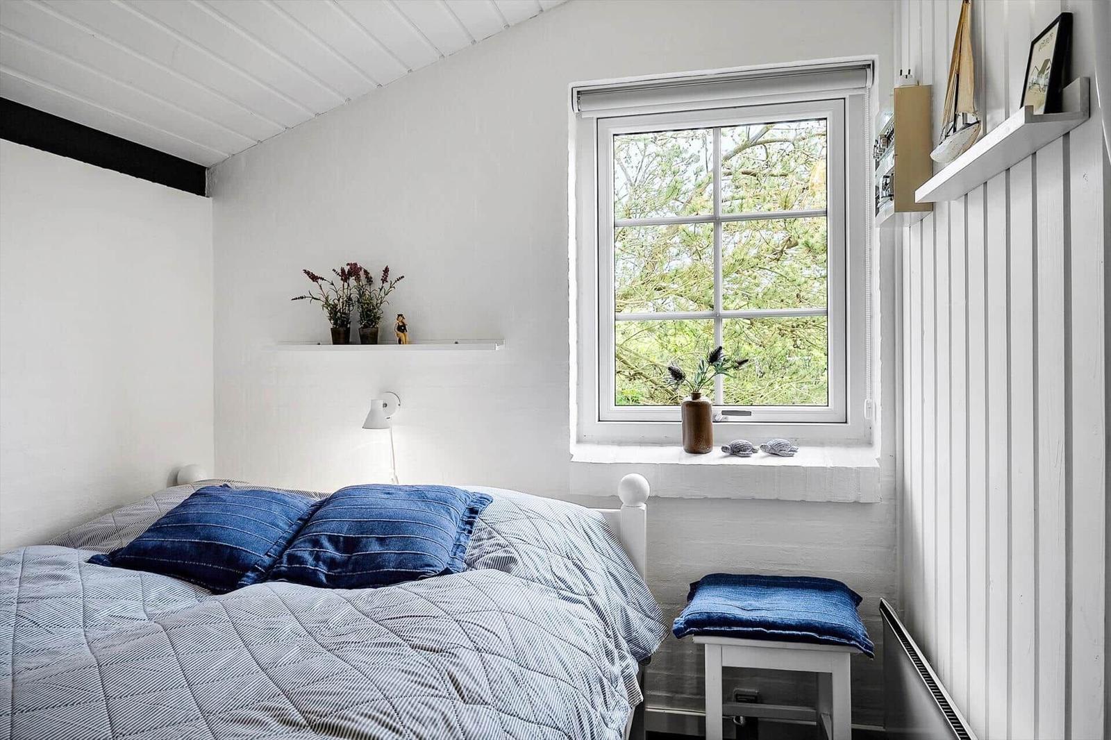 Schlafzimmer mit Bett, Fenster und Schreibtisch. Wandregal mit Pflanzen und Dekoration.