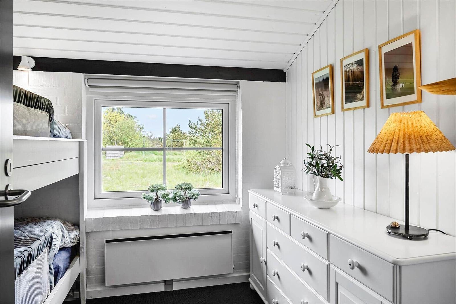 Zimmer mit Doppelstockbett, Fenster mit Blick auf Grünfläche und weißer Schrank.