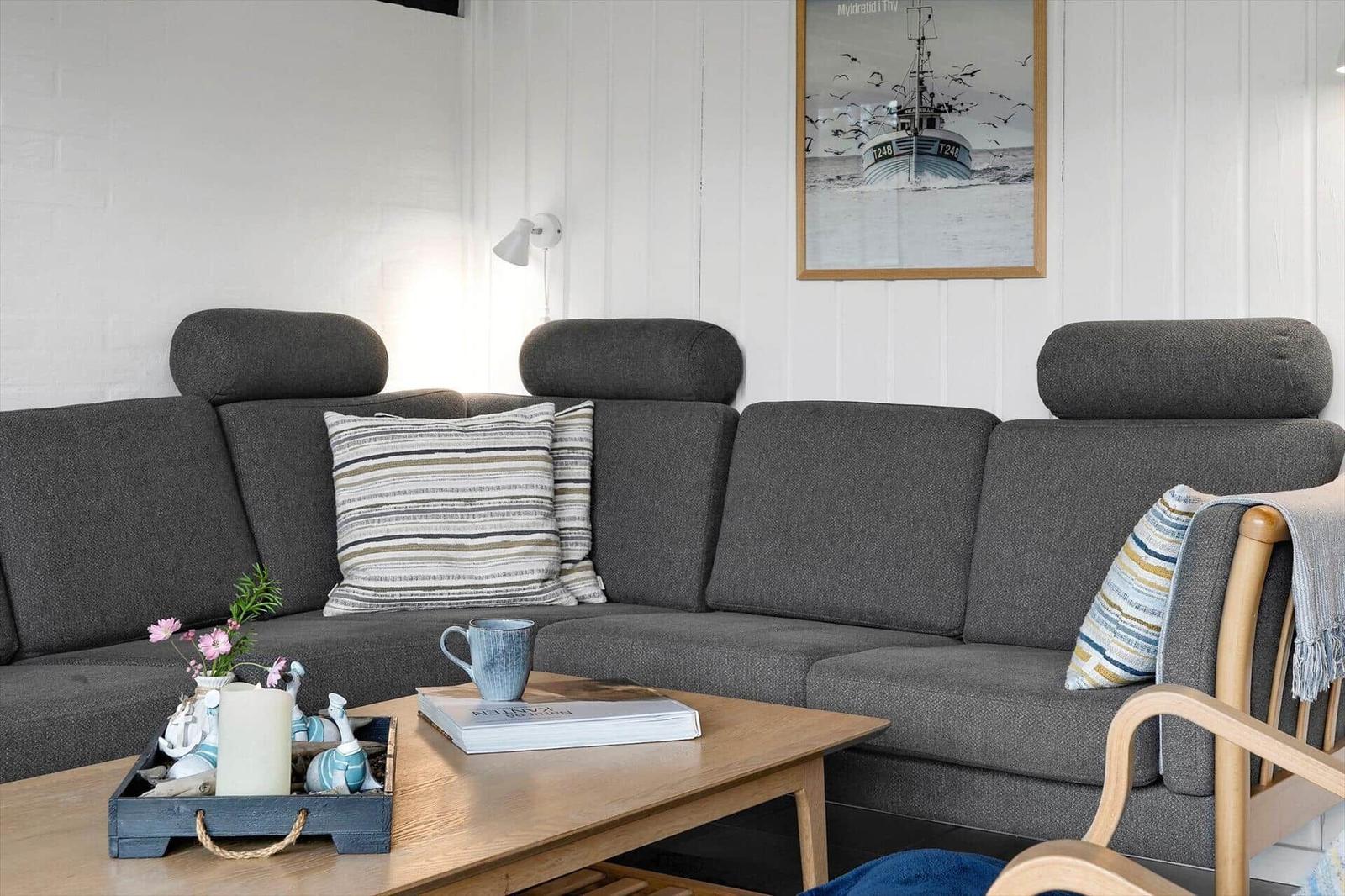 Ein Wohnzimmer mit grauem Sofa, Holztisch und Wandbild eines Bootes.