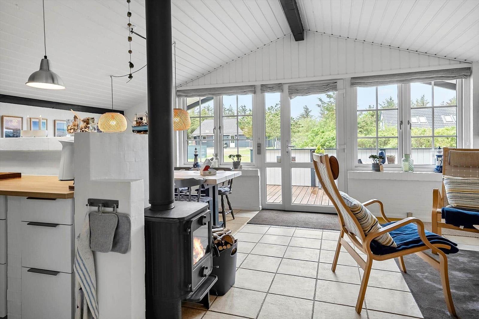 Küche mit Holztisch, Kamin und Blick auf Balkon. Holzstühle und Fenster mit Blick auf Garten.