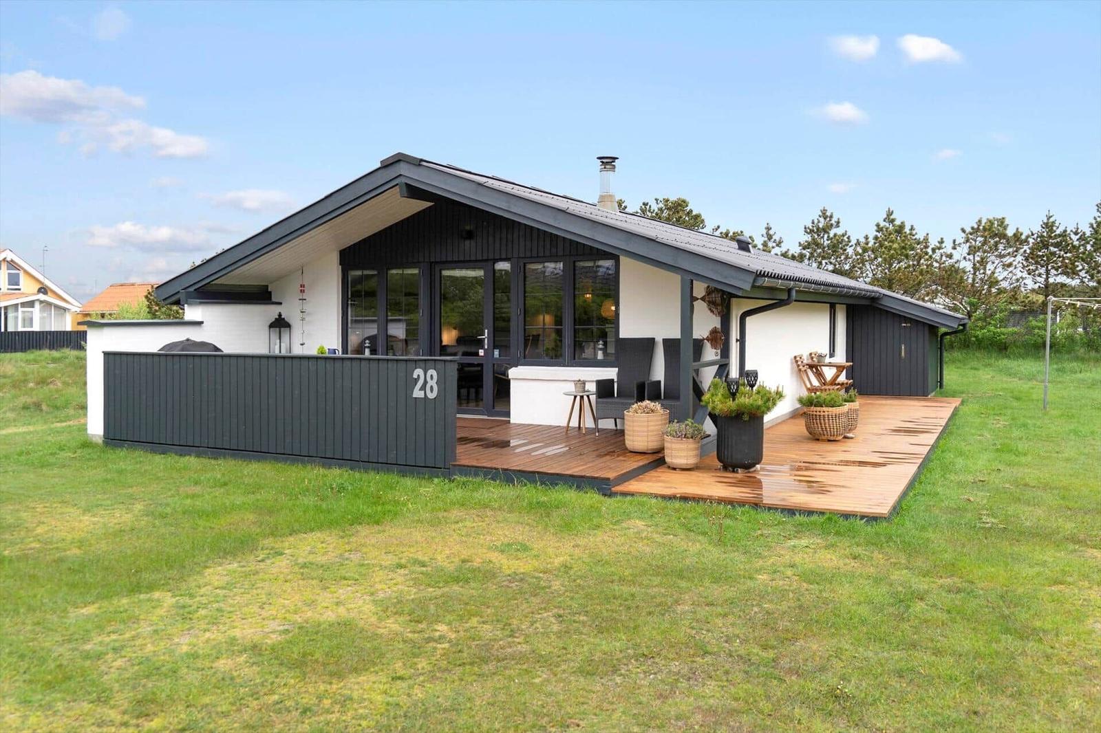 Moderne Ferienhaus mit Holzterrasse und Garten. Hausnummer 28. Sicht auf Wohnbereich und Außenterrasse.