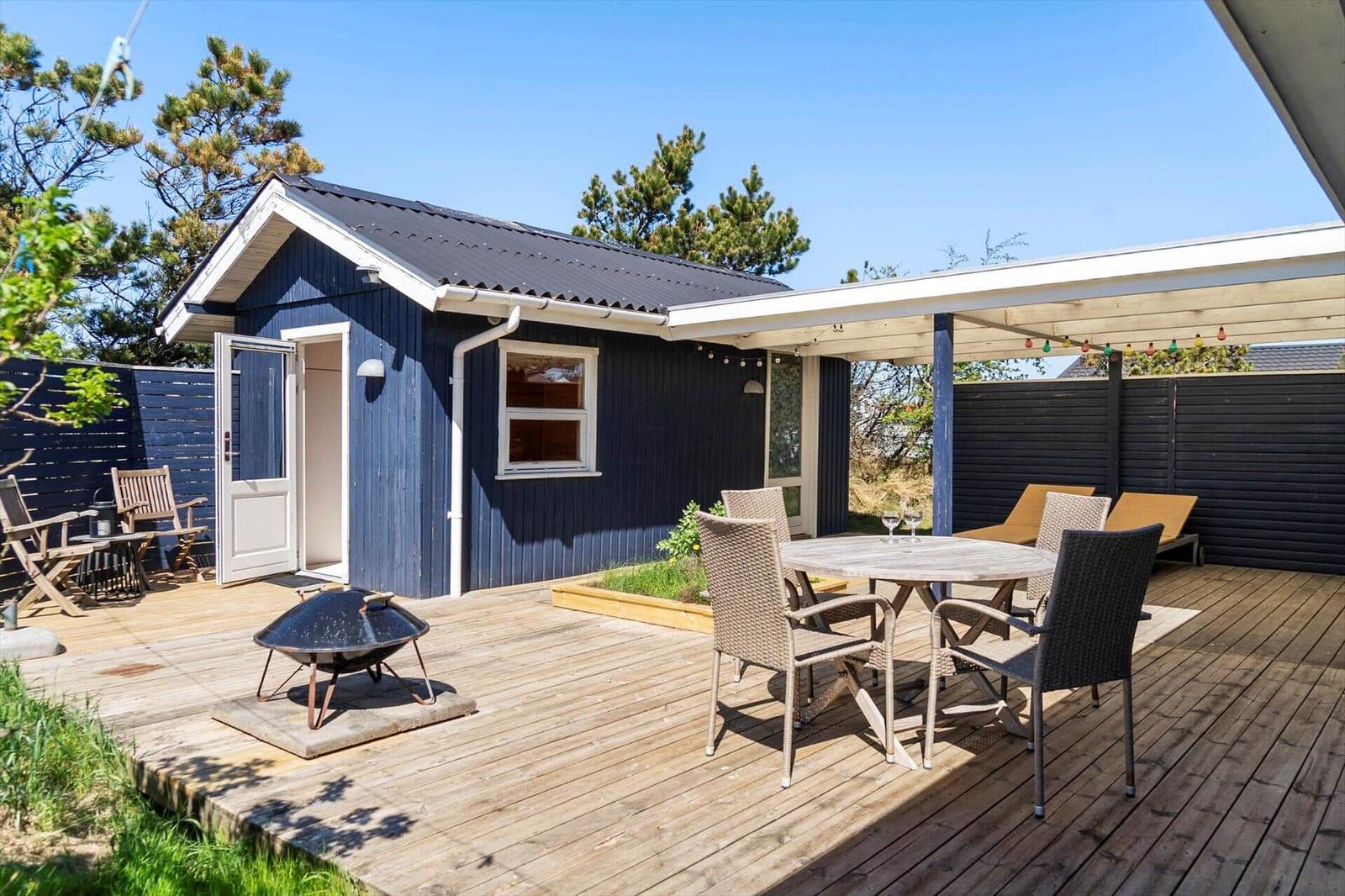 Blauer Holzblock mit Terrasse, Grill und Sitzgelegenheiten unter freiem Himmel.
