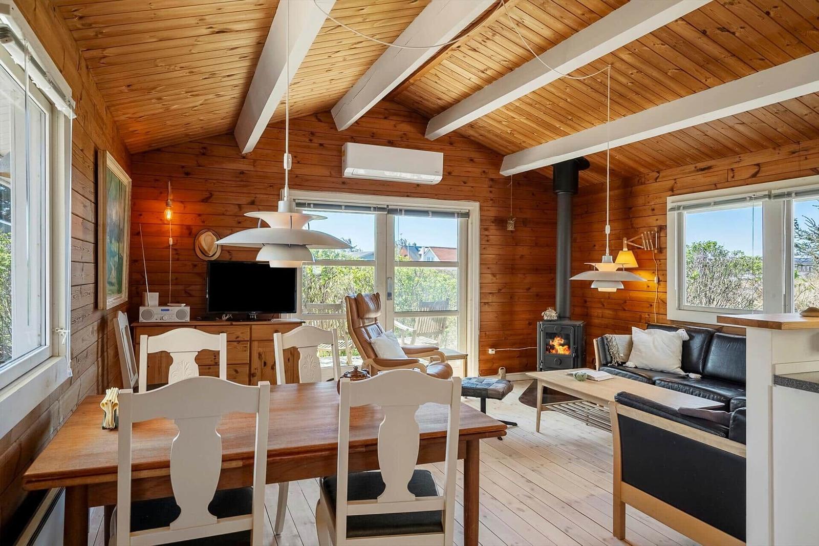 Wohn- und Essbereich mit Holzdecke, Kamin und Esszimmer mit Tisch und Stühlen.