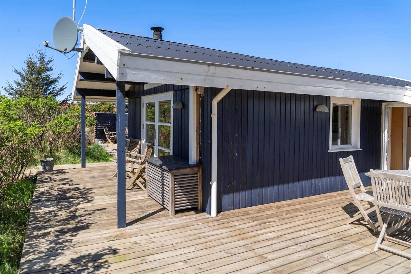 Holzterrasse mit Gartenmöbeln vor einem blauen Holzhaus mit Dachüberstand.