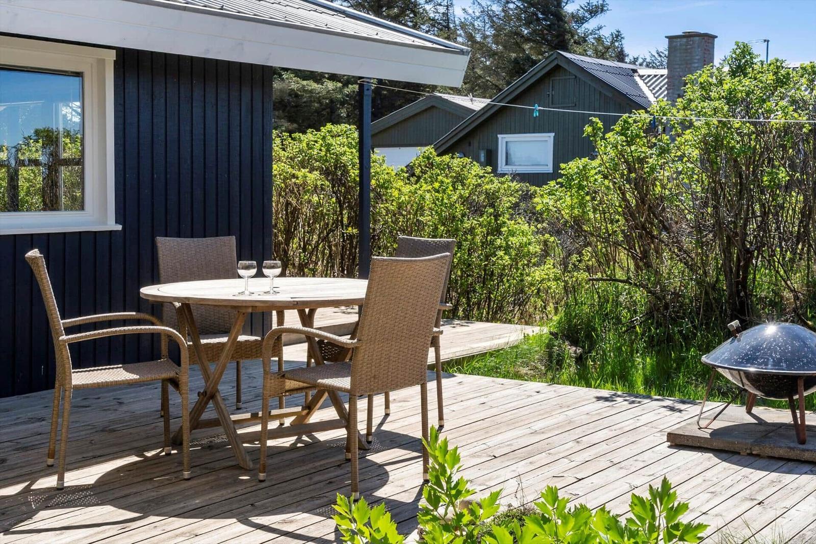 Terrasse mit Tisch, Stühlen und Grill. Hintergrund: Grünflächen und Nachbarhaus.