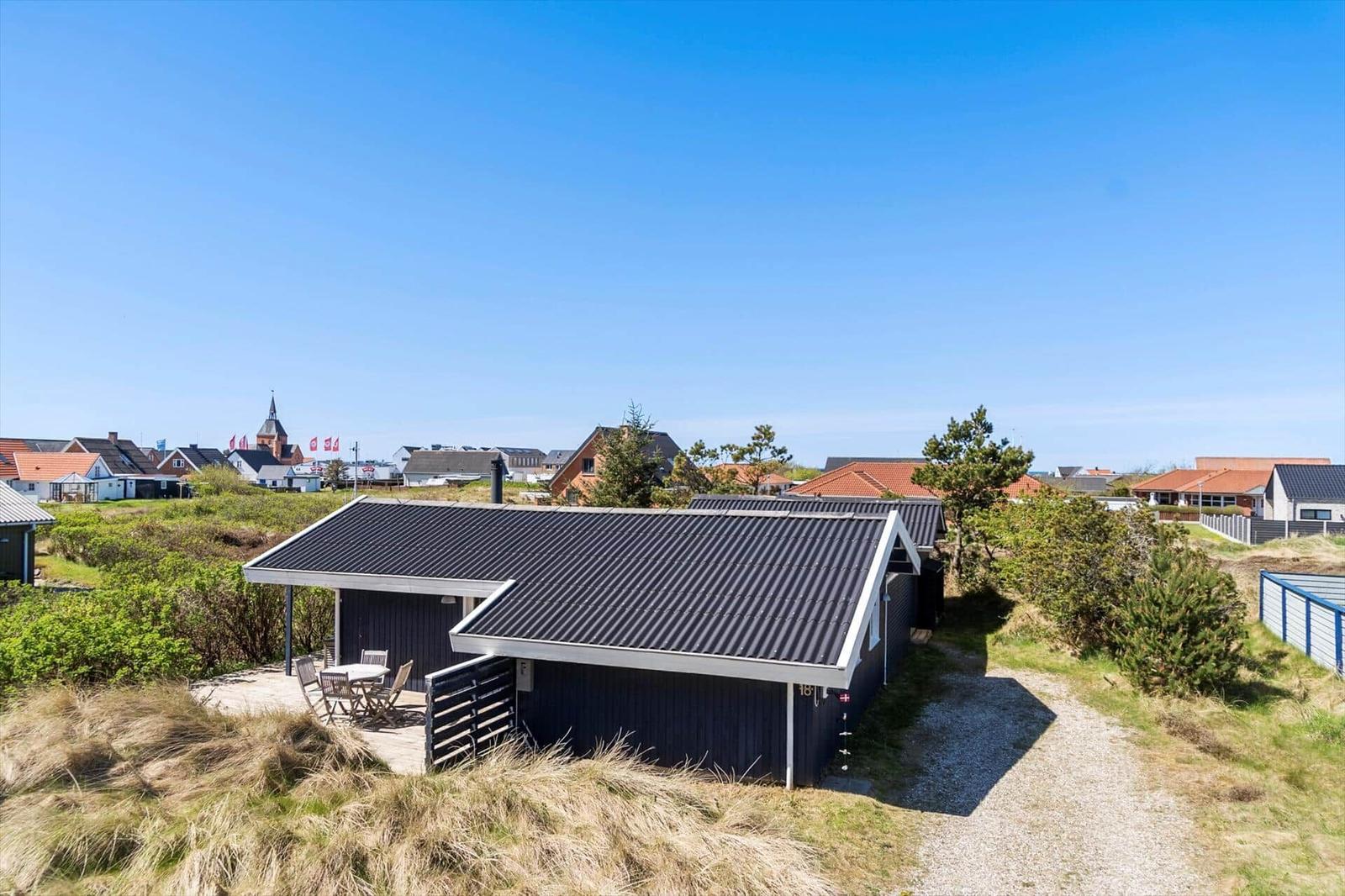 Ein dunkel gestrichenes Ferienhaus mit Terrasse und Blick auf eine Ortschaft.