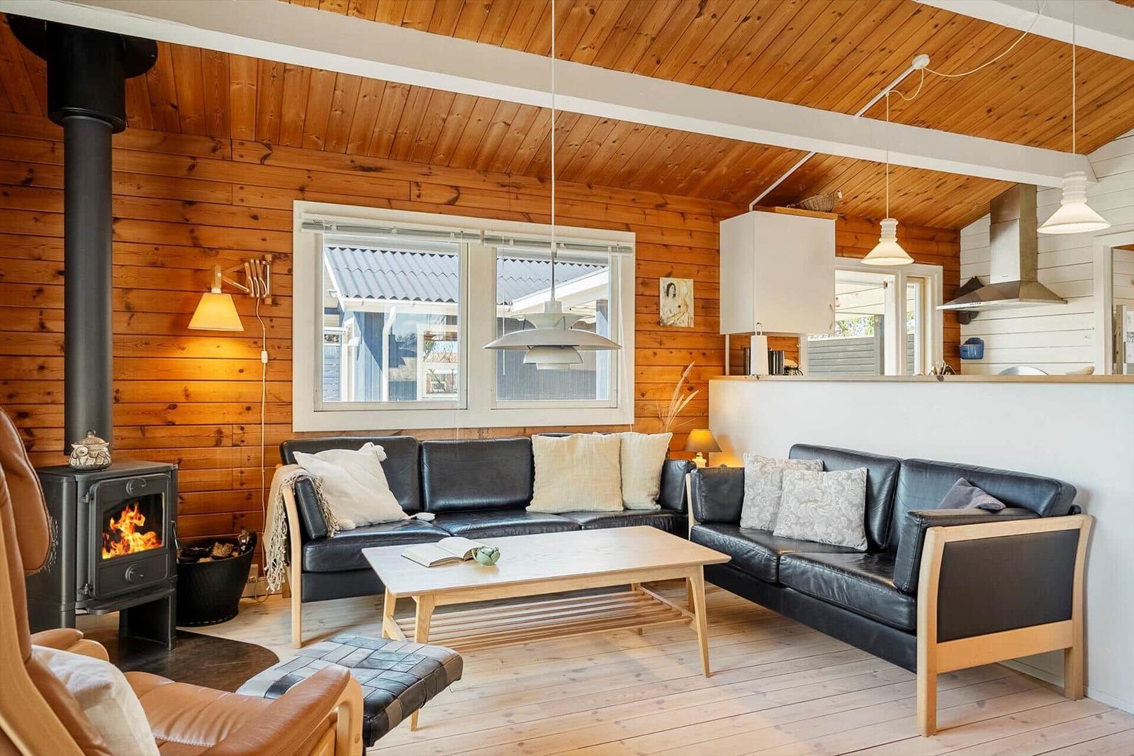Wohnzimmer mit Holzwand, Kamin und zwei schwarzen Sofas. Es gibt einen Holztisch und Fenster.